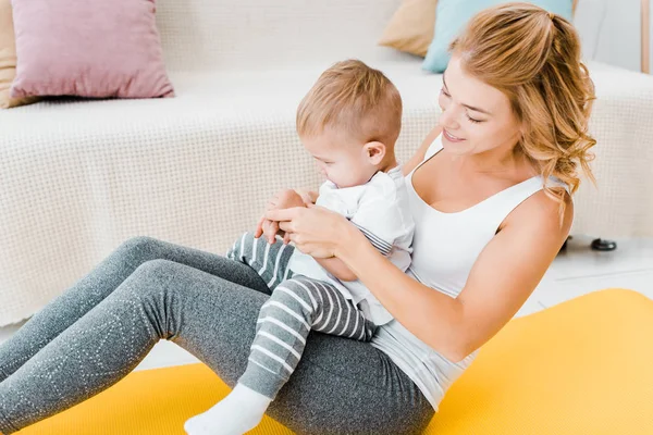 Attraktive Mutter spielt mit Kleinkind neben modernem Sofa — Stockfoto