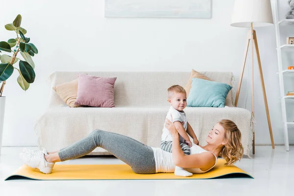 Adult woman playing with cute boy on fitness mat — Stock Photo