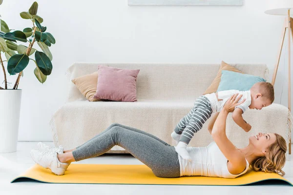 Mother lying on fitness mat and holding baby son — Stock Photo
