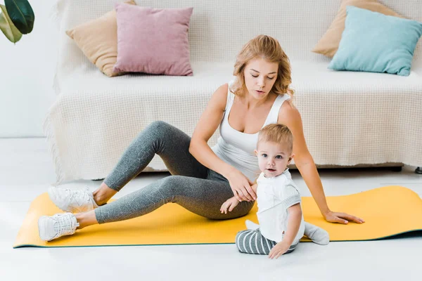 Mulher sentada no tapete de fitness e segurando bebê bonito — Fotografia de Stock
