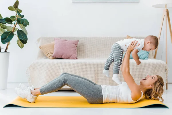 Mujer acostada en la alfombra de fitness y sosteniendo lindo niño - foto de stock