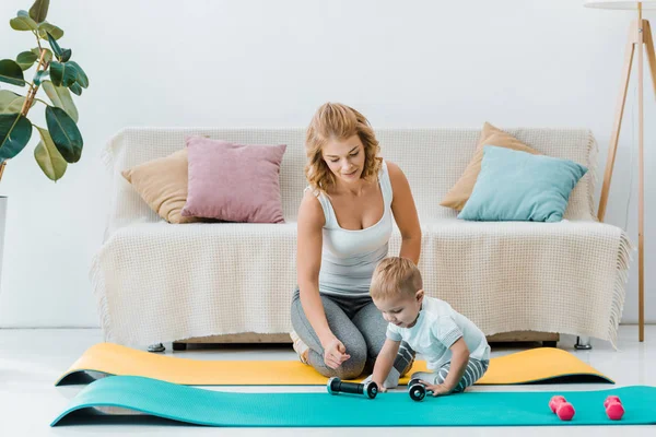 Mother looking at toddler son while boy touching dumbbells — Stock Photo