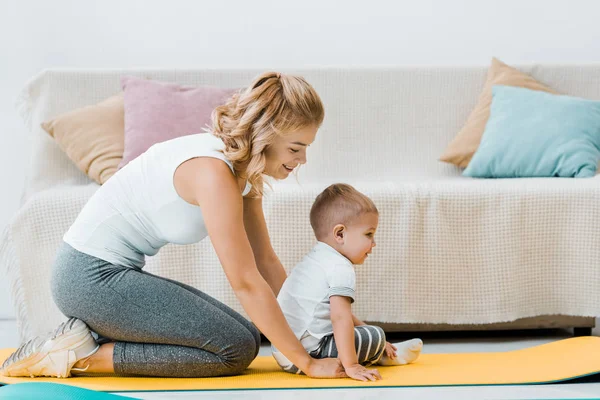 Mãe sentada no tapete de fitness e sorrindo atrás da criança — Fotografia de Stock