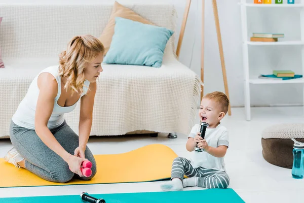 Mother looking at adorable child son while boy smiling and lifting weights — Stock Photo