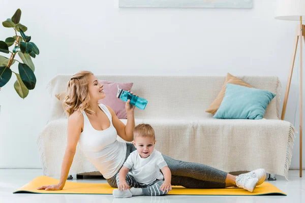 Mujer bebiendo agua y haciendo ejercicio cerca del niño - foto de stock