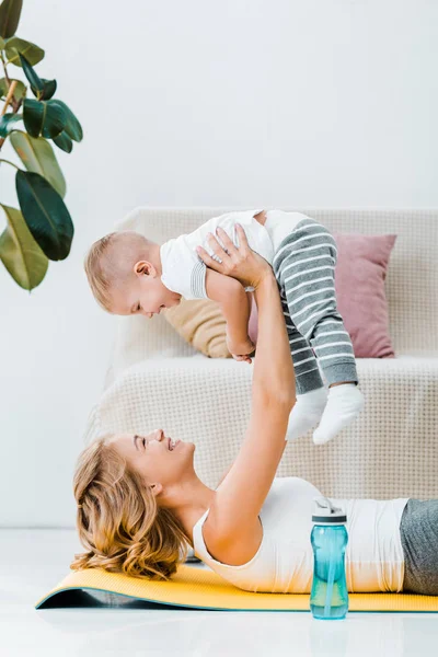 Femme couchée près de la plante et élevant adorable enfant au-dessus de la tête — Photo de stock