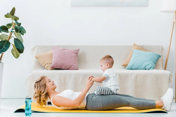 Frau liegt auf Fitnessmatte und spielt mit süßem Kleinkind-Sohn — Stockfoto