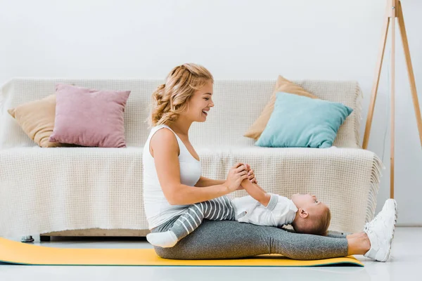 Woman sitting on fitness mat and playing with toddler son — Stock Photo