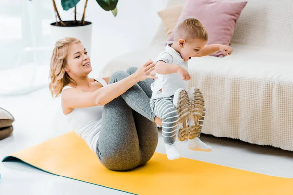 Femme couchée sur tapis de fitness tout en tenant adorable bébé fils — Photo de stock