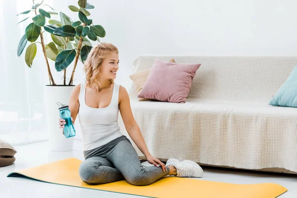 Woman sitting on fitness mat and drinking water from sport bottle — Stock Photo