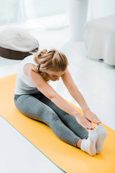 Mulher em sportswear fazendo exercício de alongamento no tapete de fitness amarelo em casa — Fotografia de Stock