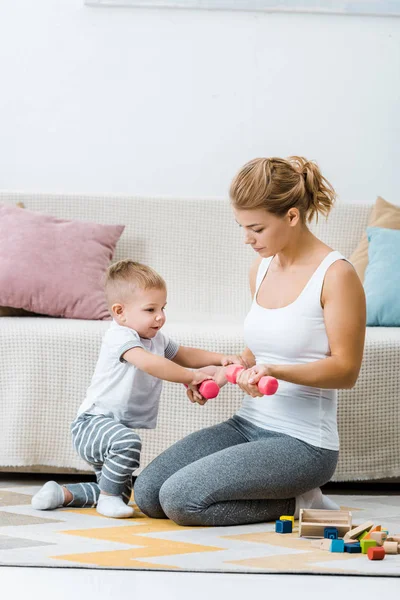 Attrayant femme tenant haltères avec mignon tout-petit garçon dans le salon — Photo de stock