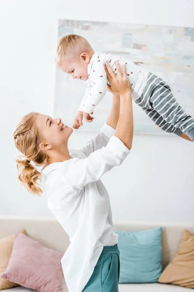 Attraktive Frau zieht Kleinkind groß und lächelt im Wohnzimmer — Stockfoto