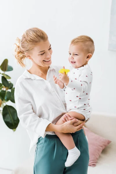 Donna sorridente in piedi e tenendo in braccio il figlio bambino a casa — Foto stock