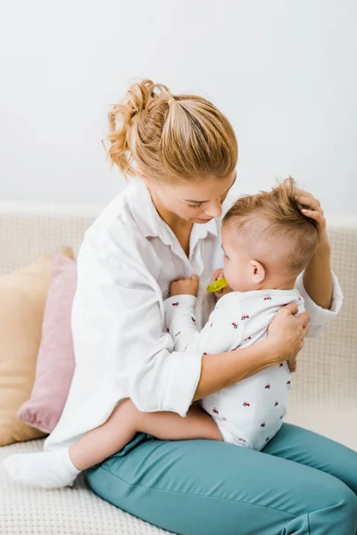 Mère assis sur canapé et étreignant tout-petit fils dans le salon — Photo de stock