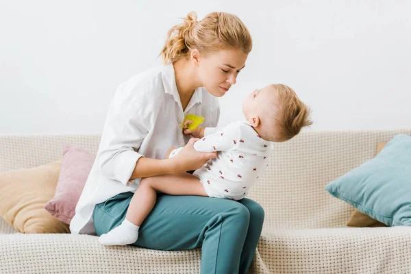 Mutter mit geschlossenen Augen sitzt auf Sofa und hält Kleinkind im Wohnzimmer — Stockfoto