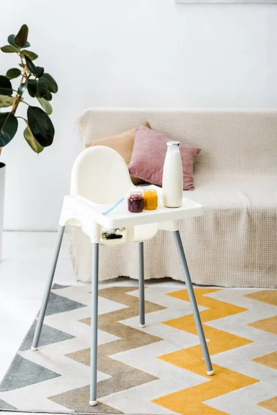 Baby food jars and milk bottle on white highchair in living room — Stock Photo