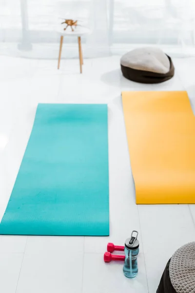 Blue and yellow fitness mats, dumbbells and sport bottle with water on floor at home — Stock Photo