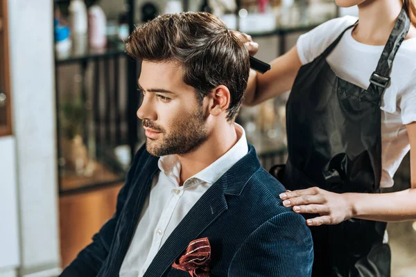 Plan recadré de coiffeur peigner les cheveux à beau jeune homme dans le salon de beauté — Photo de stock