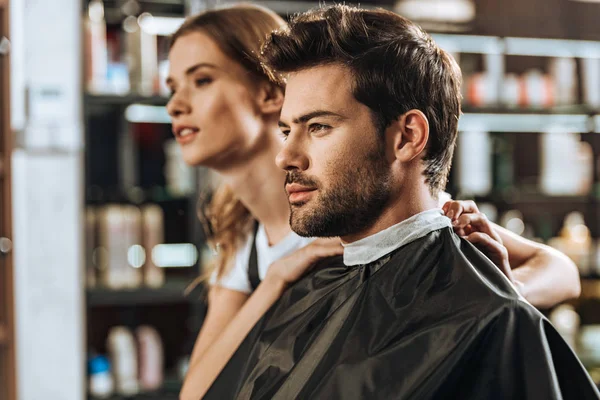 Beau jeune homme et belle coiffeuse regardant loin dans le salon de beauté — Photo de stock