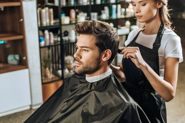 Cropped shot of hairdresser combing hair to handsome young man in beauty salon — Stock Photo