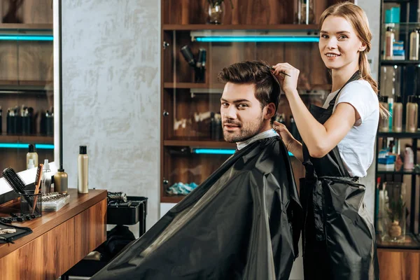 Young hairstylist and male client smiling at camera in beauty salon — Stock Photo