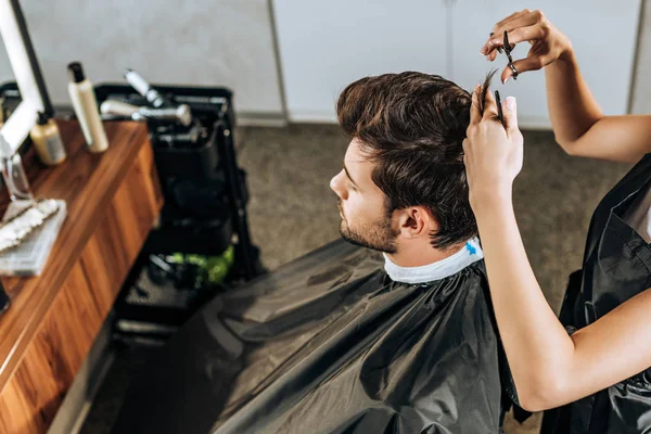 Alto ángulo vista de peluquero corte de pelo a guapo joven en salón de belleza - foto de stock