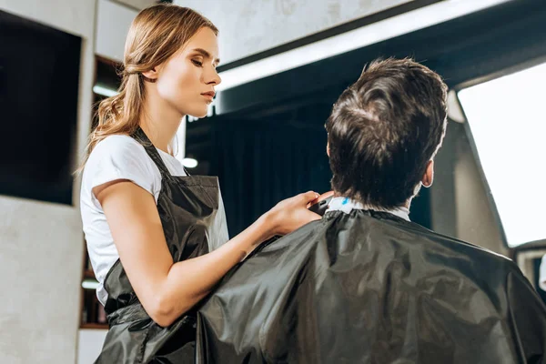 Young hairdresser using electric hair clipper while working with client in beauty salon — Stock Photo