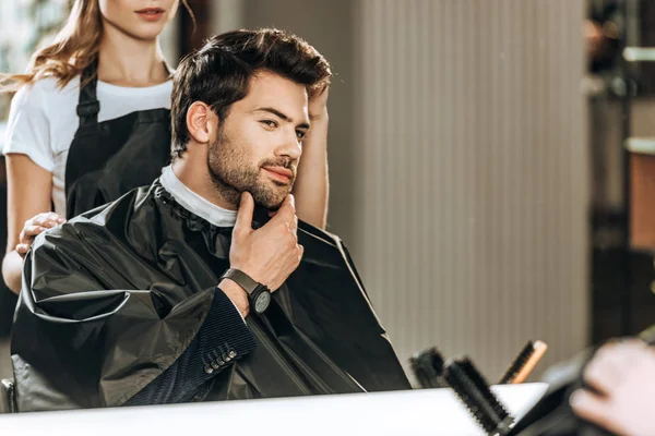 Corte tiro de cabeleireiro fazendo penteado para homem bonito olhando para o espelho no salão de beleza — Fotografia de Stock