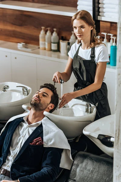 Visão de alto ângulo de cabelo jovem cabeleireiro lavagem de cabelo para cliente bonito no salão de beleza — Fotografia de Stock