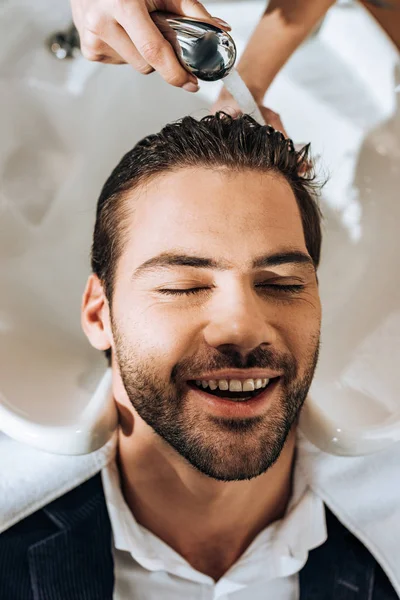 Plan recadré de coiffeur laver les cheveux à heureux beau jeune homme dans le salon de beauté — Photo de stock