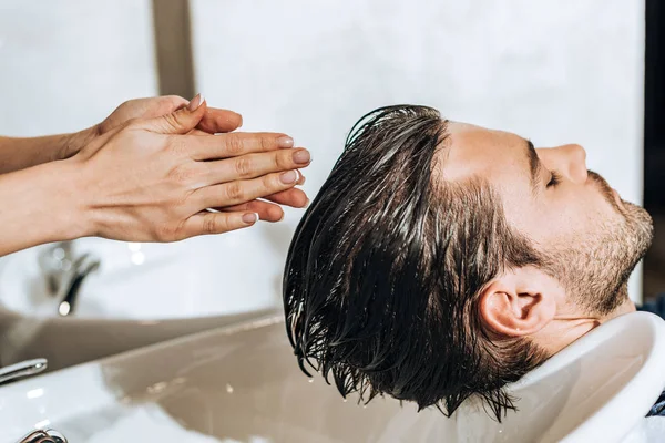 Mains de jeune coiffeur laver les cheveux au client masculin dans le salon de beauté — Photo de stock