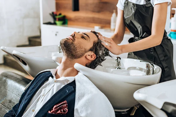 Abgeschnittene Aufnahme eines Friseurs, der einem hübschen männlichen Kunden im Schönheitssalon die Haare wäscht — Stockfoto