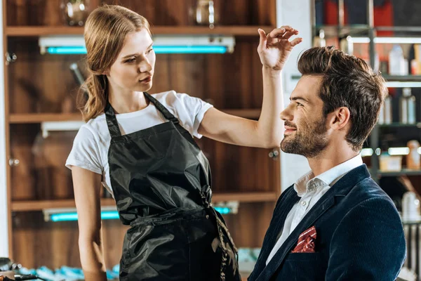 Beautiful young hairstylist looking at handsome smiling man in beauty salon — Stock Photo