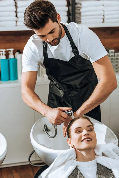 Bonito jovem cabeleireiro lavar o cabelo para sorrir jovem mulher no salão de beleza — Fotografia de Stock