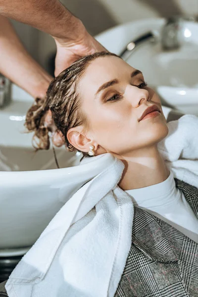 Primer plano vista parcial de peluquero lavando el cabello a chica atractiva en salón de belleza — Stock Photo