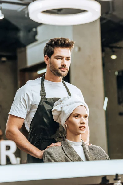 Fille avec serviette sur la tête et jeune coiffeur regardant miroir dans le salon de beauté — Photo de stock