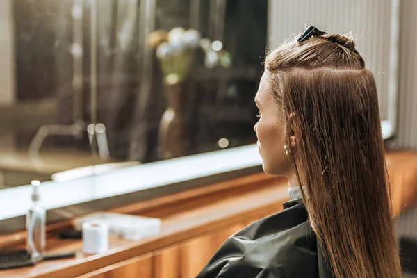 Profil der schönen jungen Frau, die im Schönheitssalon sitzt und in den Spiegel schaut — Stockfoto