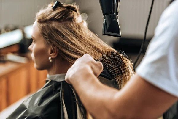 Plan recadré de coiffeur séchage des cheveux à la fille attrayante dans le salon de beauté — Photo de stock