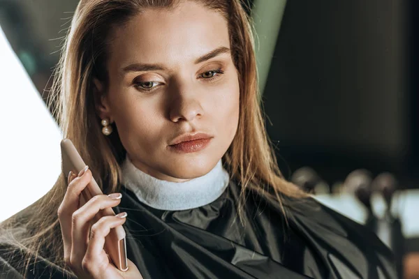 Beautiful young woman using smartphone in beauty salon — Stock Photo