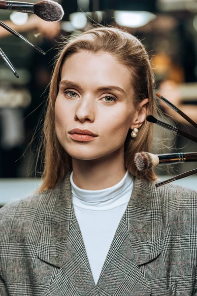 Hermosa mujer joven mirando a la cámara, mientras que los estilistas que aplican maquillaje - foto de stock