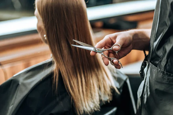 Plan recadré de coiffeur tenant des ciseaux et jeune femme visitant salon de beauté — Photo de stock