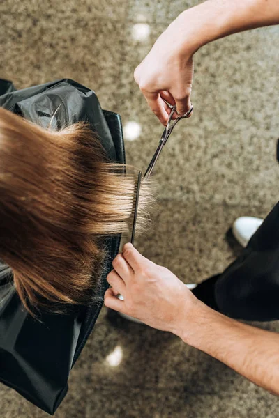 Partial top view of cropped shot of hairdresser cutting hair to young woman in beauty salon — Stock Photo