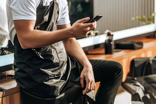 Plan recadré de jeune coiffeur masculin en utilisant smartphone dans le salon de beauté — Photo de stock