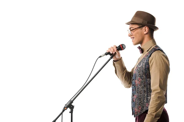 Side view of smiling mixed race male musician in hat singing in microphone isolated on white — Stock Photo