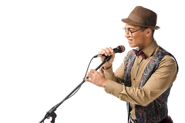 Side view of smiling mixed race young man in hat singing in microphone isolated on white — Stock Photo