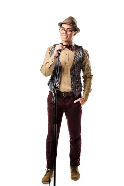 Alegre joven mixto hombre de raza en elegante sombrero y gafas cantando en micrófono aislado en blanco - foto de stock