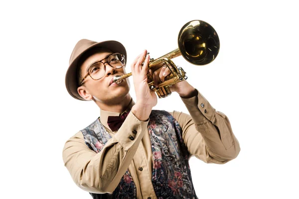 Joven hombre de raza mixta en elegante sombrero y gafas tocando en trompeta aislado en blanco - foto de stock