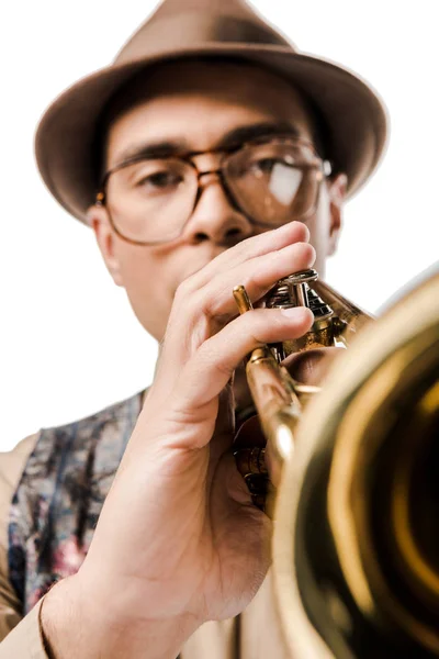 Vista de cerca del músico masculino de raza mixta con sombrero elegante y anteojos tocando en trompeta aislado en blanco - foto de stock