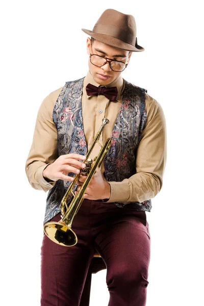 Joven jazzman masculino sosteniendo trompeta y sentado en silla aislado en blanco - foto de stock